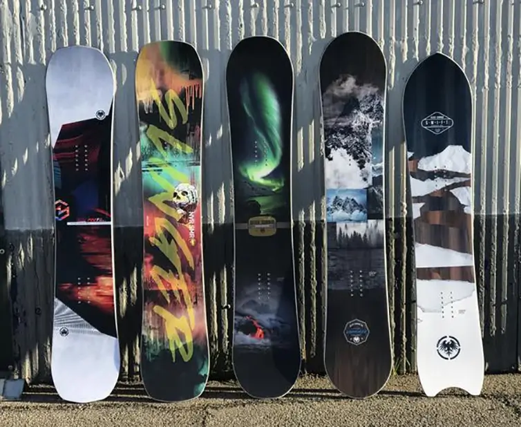 Five snowboards lined up in a row lent up against a metal wall.