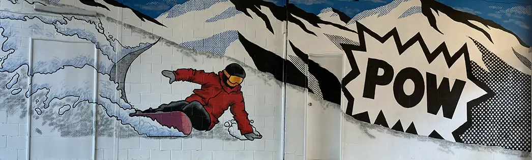 Hand-painted mural on a brick wall of a snowboarder going down the hill next to the Cherri Pow logo.